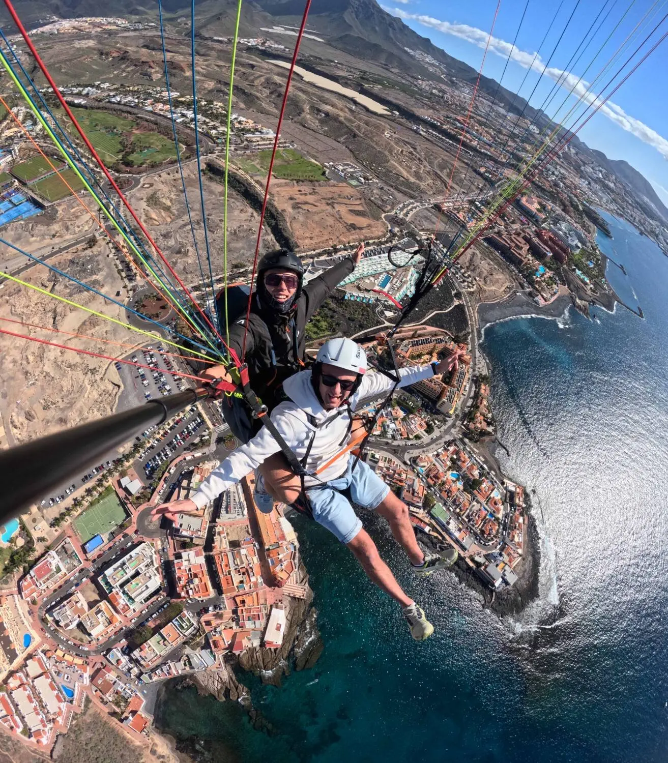Tandem paraglider over La Caleta and Costa Adeje, pilot and passenger smiling above the coast