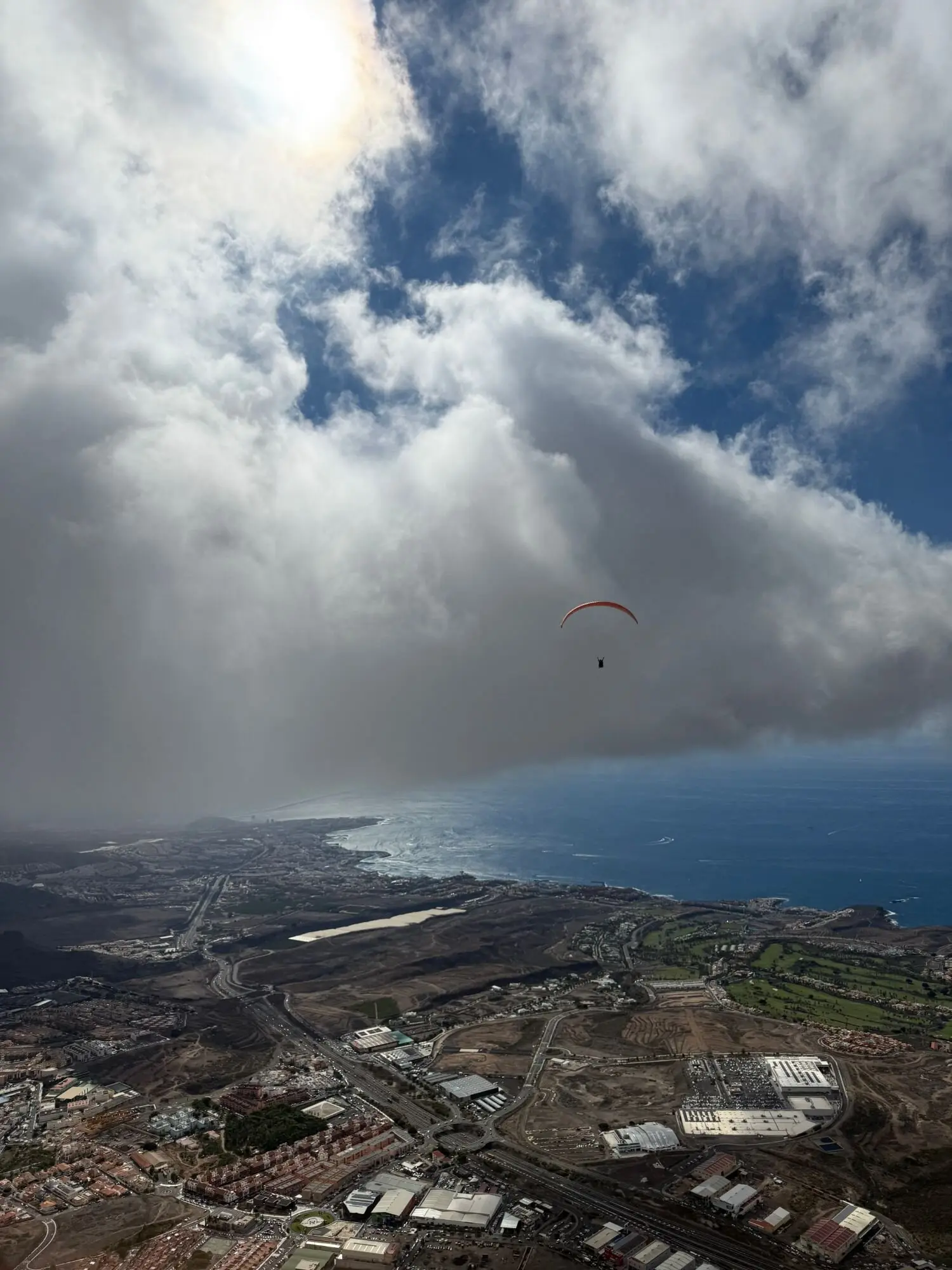 Lone paraglider gliding between clouds above the coast of south Tenerife