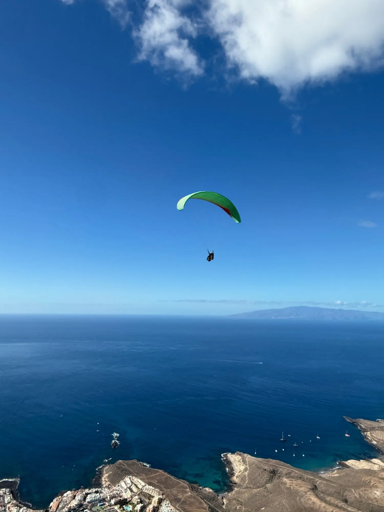 Green paraglider wing over the deep blue Atlantic off Tenerife, La Gomera on the horizon