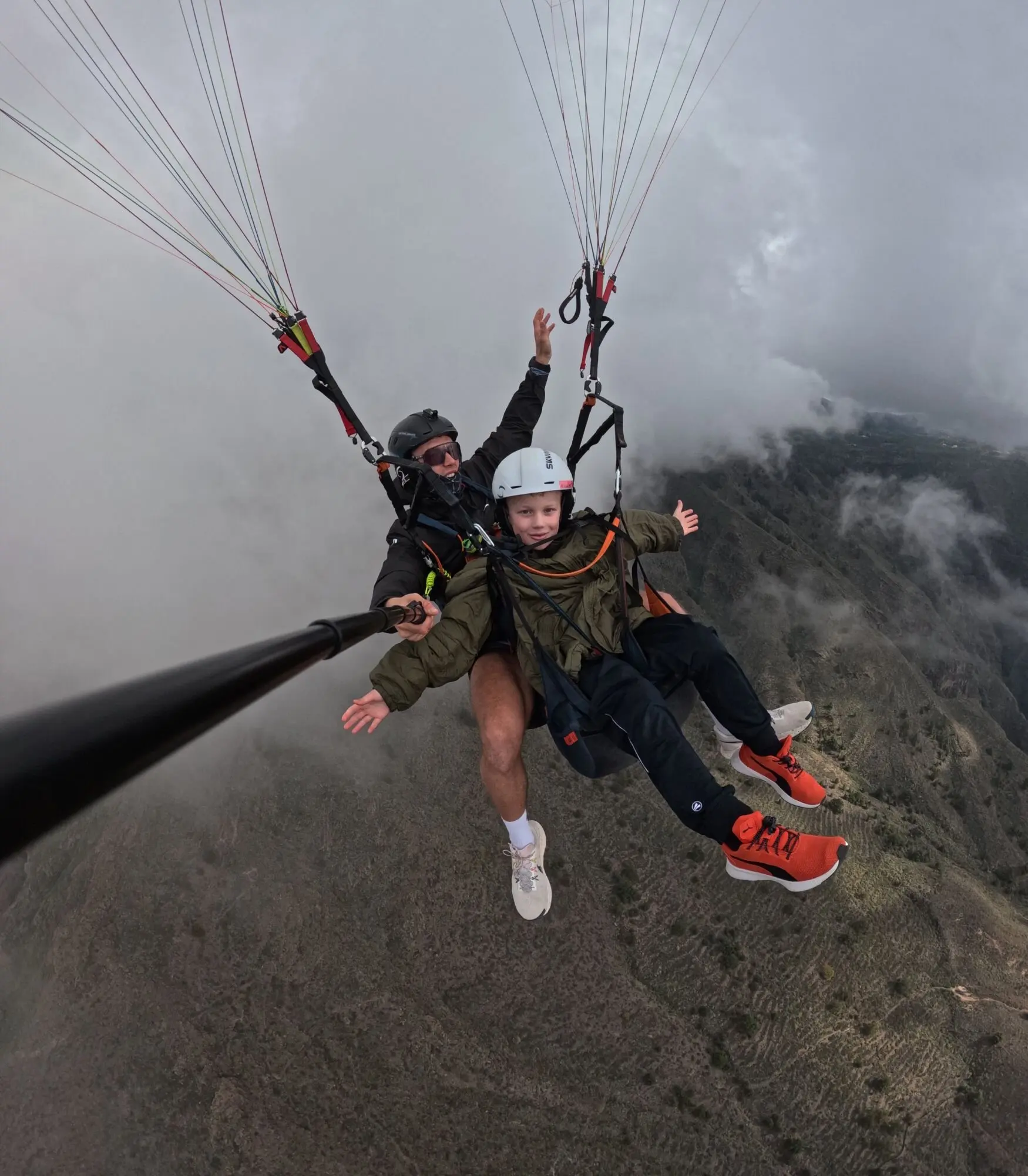 Child passenger in a tandem paraglider with the pilot above the Adeje mountains