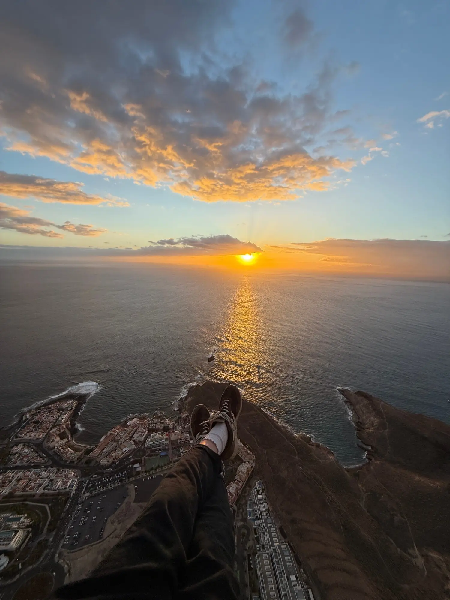 Passenger's feet over La Caleta at sunset, the sun setting into the sea