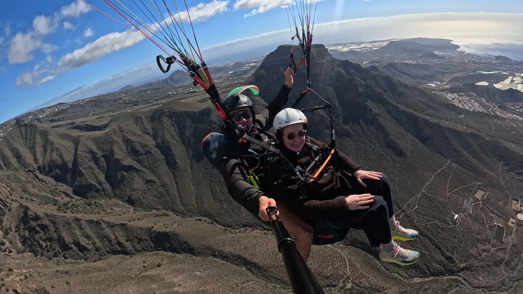 Tandem paraglider over La Caleta and Costa Adeje, pilot and passenger smiling above the coast